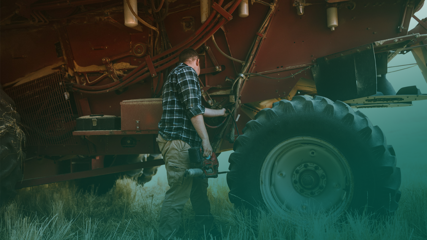 A man wearing a plaid shirt tending to a red tractor